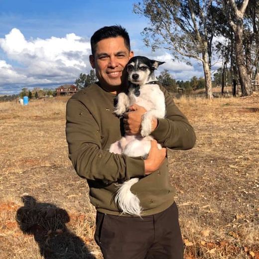 A smiling person in an open field holding Scruffy, a small black and white terrier, in their arms