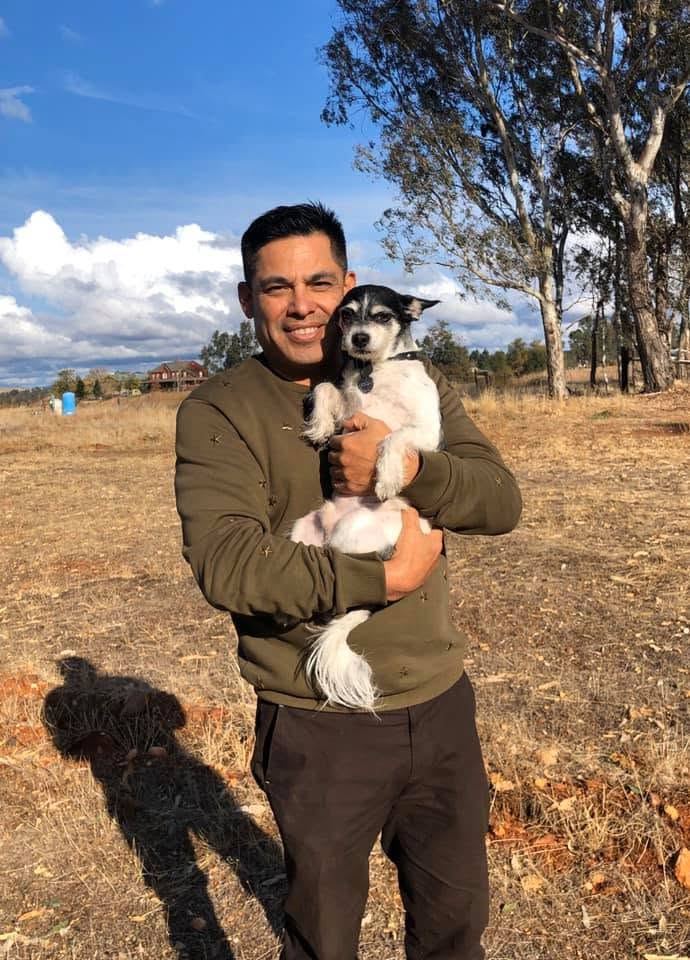 Scruffy, a small black and white terrier, held in the arms of a smiling person in an open field